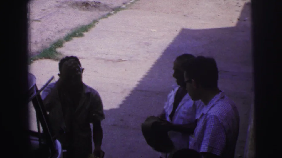 A shaded 1967 Brazil street moment shows one man looking upward while two others stand nearby, one holding a dark hat.