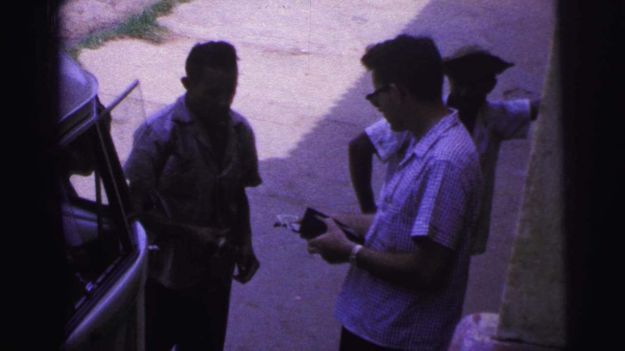Three adult men stand near a vehicle while two handle papers or money in strong sunlight and shade.