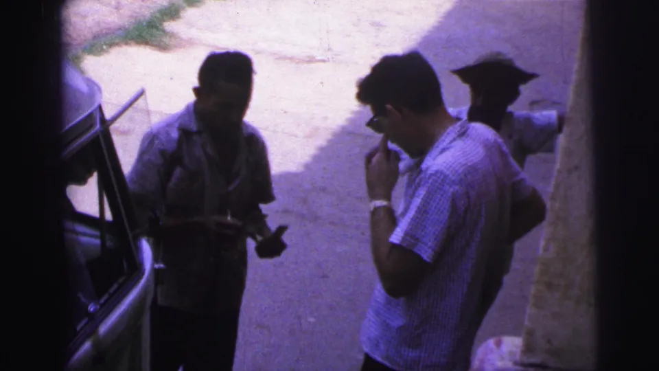 In 1967 Brazil footage, the roadside exchange continues as one man brings a cigarette to his mouth and another holds papers or cash.
