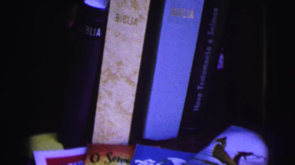 1967 Brazil 8mm frame showing Portuguese Bibles and religious pamphlets in a dim close-up arrangement.