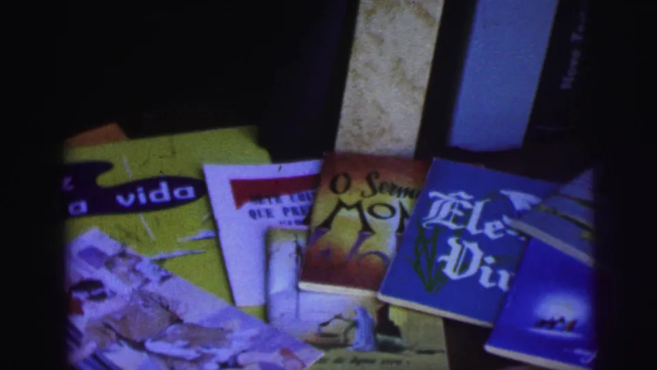 1967 Brazil home-movie frame of religious pamphlets and small books arranged on a dark surface with visible Portuguese titles.