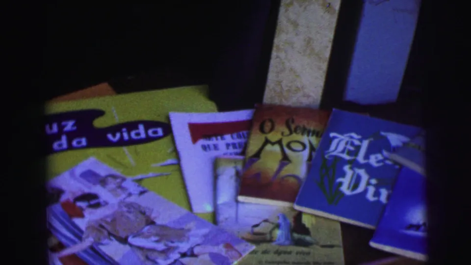 1967 Brazil home-movie frame showing Portuguese-language printed covers on a tabletop before the work yard sequence.