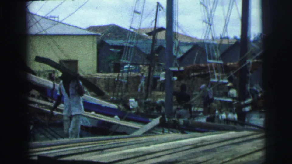 1967 Brazil footage shows workers carrying large wooden pieces in a lumber or boatyard with boats and rigging behind them.