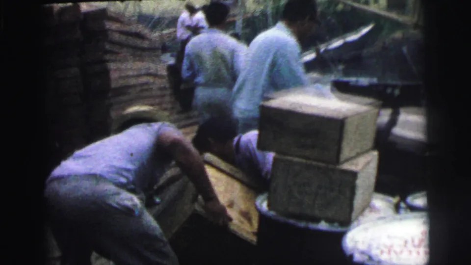 Several adult men work around wooden crates on a Brazilian waterfront dock in 1967, with stacked boxes in the foreground.