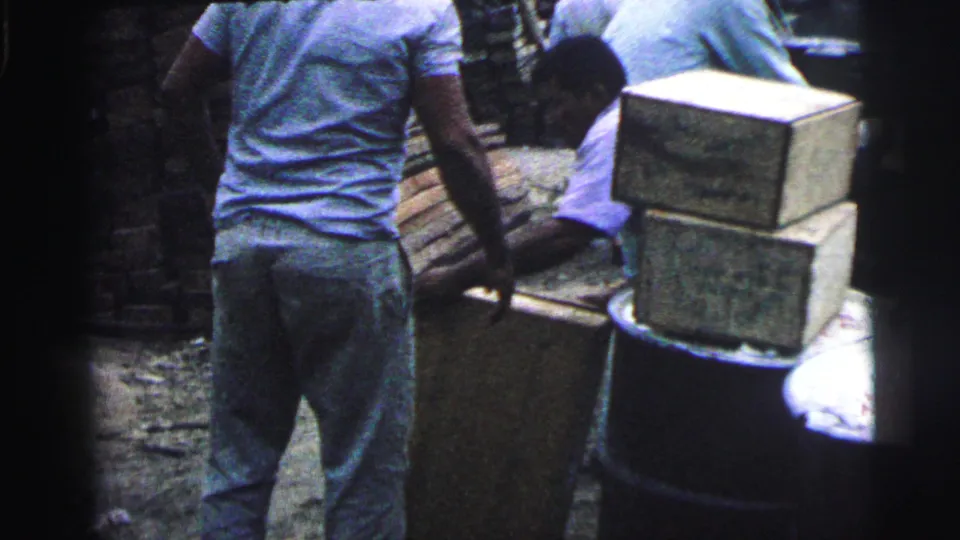 Worker in a light shirt stands near stacked wooden crates and barrels in a Brazil port scene from 1967.