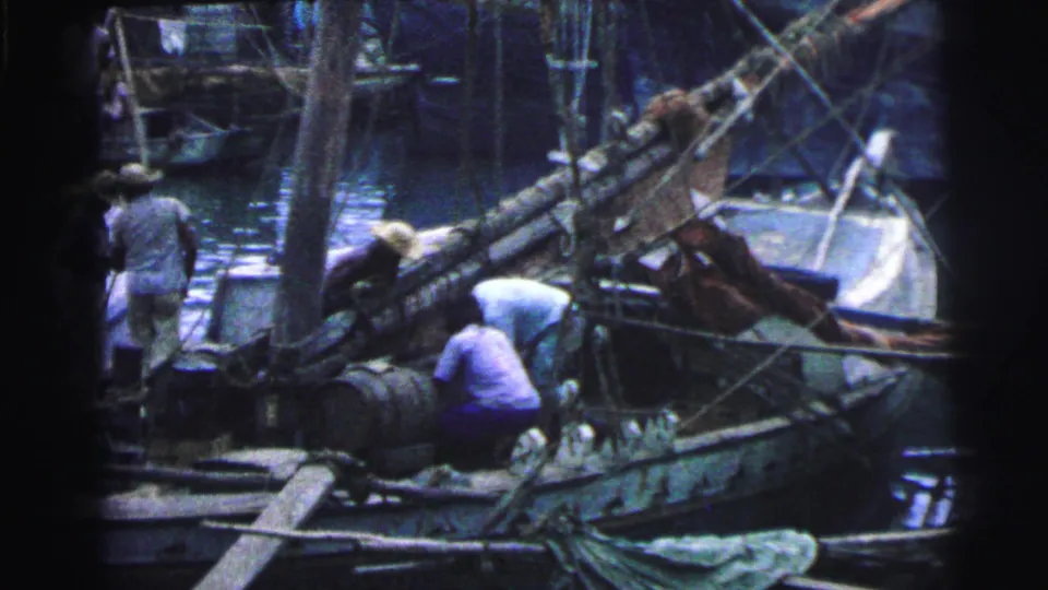 1967 Brazil 8mm frame showing workers on a crowded fishing boat with barrels, rigging, masts, and water in the background.
