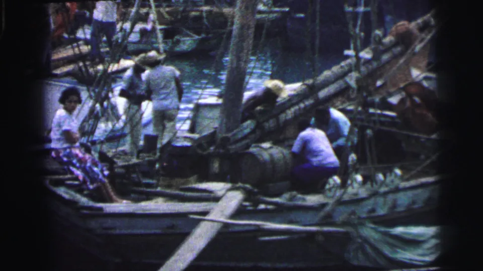 1967 Brazil 8mm frame showing a seated woman near the bow and workers preparing boat gear amid ropes, barrels, and masts.