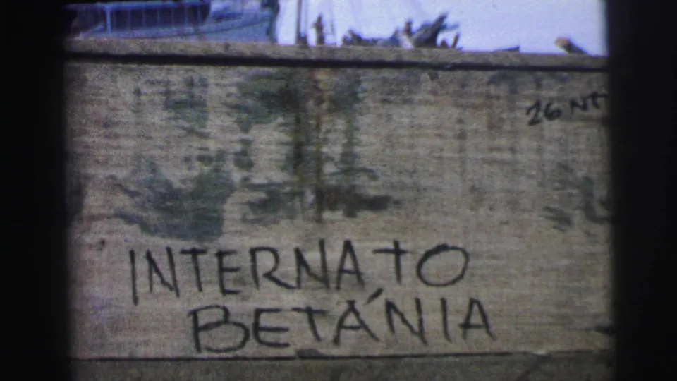 1967 Brazil 8mm frame showing a weathered wall marked “INTERNATO BETÂNIA,” with a small boat and water partly visible beyond it.