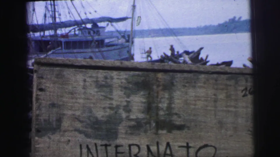1967 Brazil 8mm frame showing a moored boat and shoreline activity above a wall with the lower word “INTERNATO” partly visible.