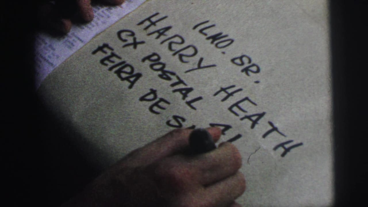 Hand with black marker writing on a paper-wrapped package with partial address text visible.