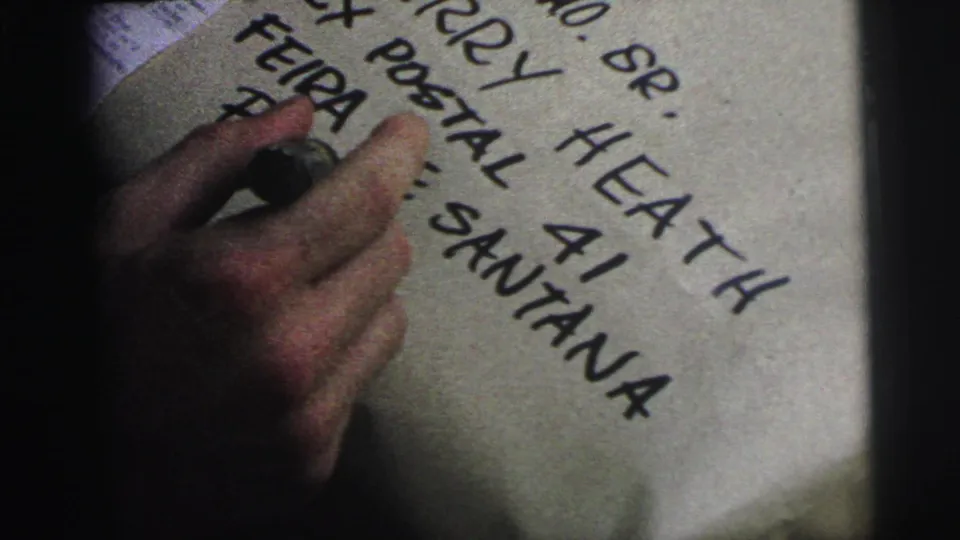 Close frame shows a hand and marker over handwritten package text including postal and Bahia address details.