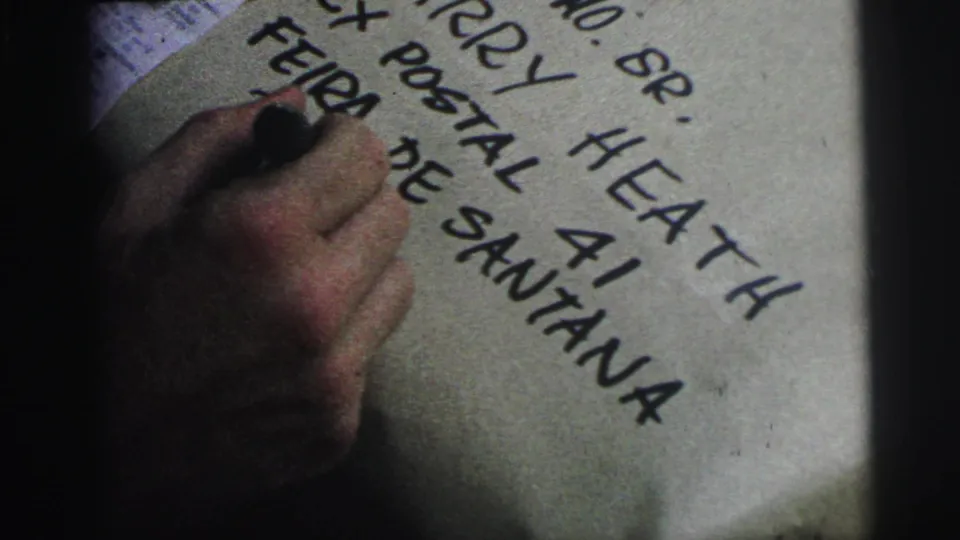 Close 8mm frame of a hand writing near visible Feira de Santana text on a paper-wrapped package in Brazil.