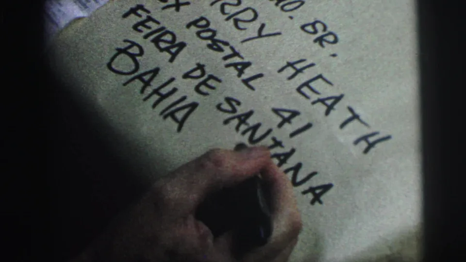 Final close frame shows the hand and marker near large handwritten Bahia text on the addressed package.