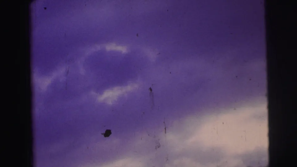 Brazil 1967 8mm view of purple-blue clouds with a central dark border, specks, scratches, and aged film texture.