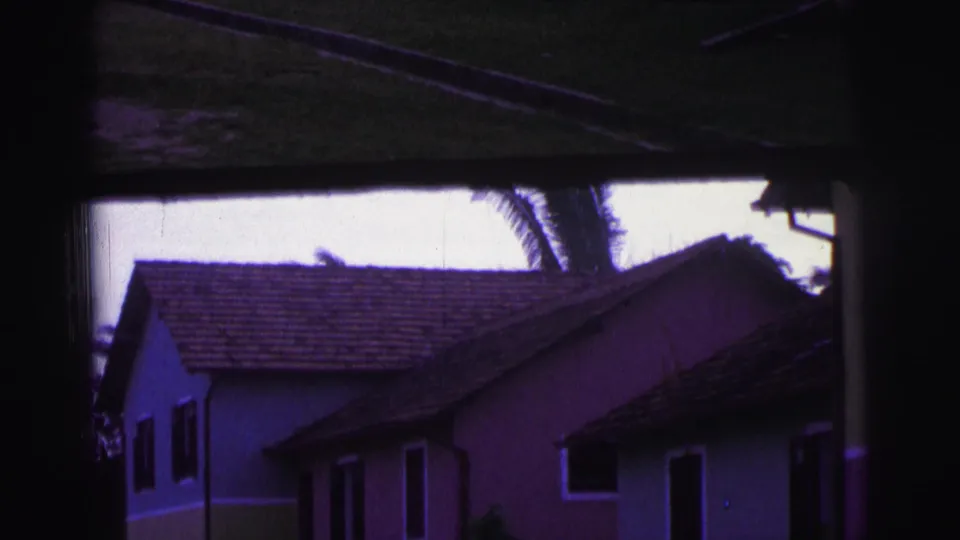 Soft 8mm view of pastel Brazilian houses, tiled roofs, shutters, lawn, and palm fronds under a purple-blue color shift.