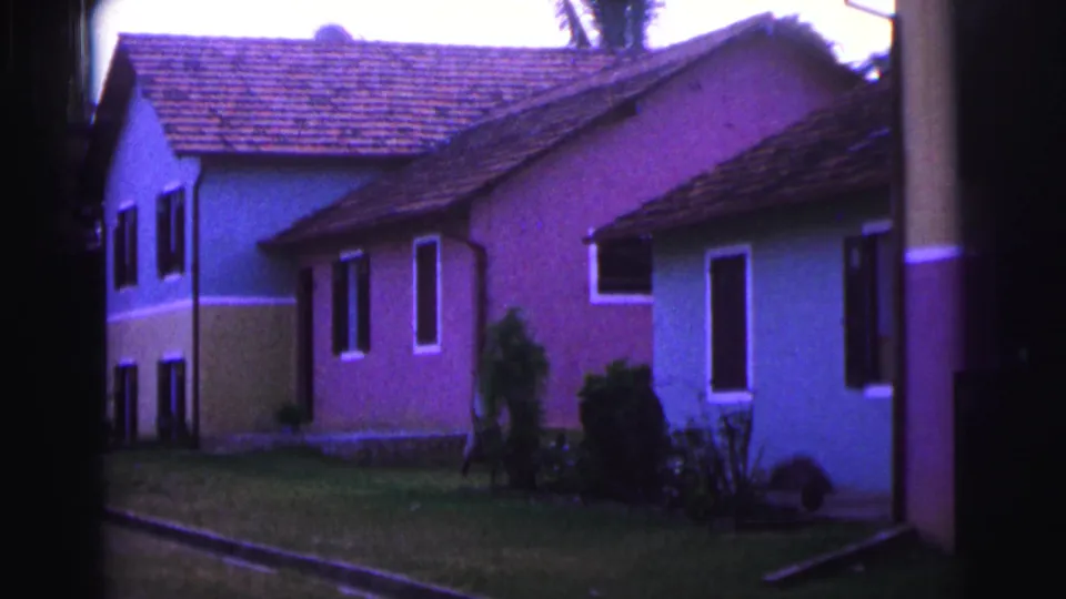 1967 Brazil 8mm view of pastel residential homes, tiled roofs, a lawn, shrubs, and palms in soft handheld framing.