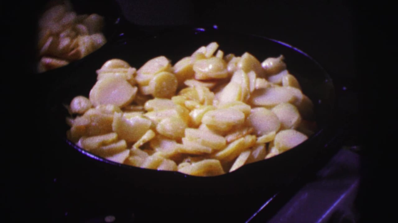 Sliced potatoes cooking in a black pan on a dim stovetop.