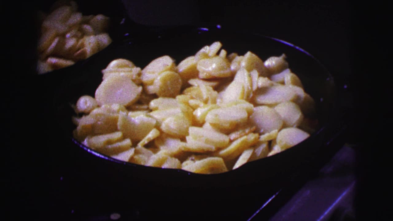Close view of sliced potatoes filling a dark pan on a stove.