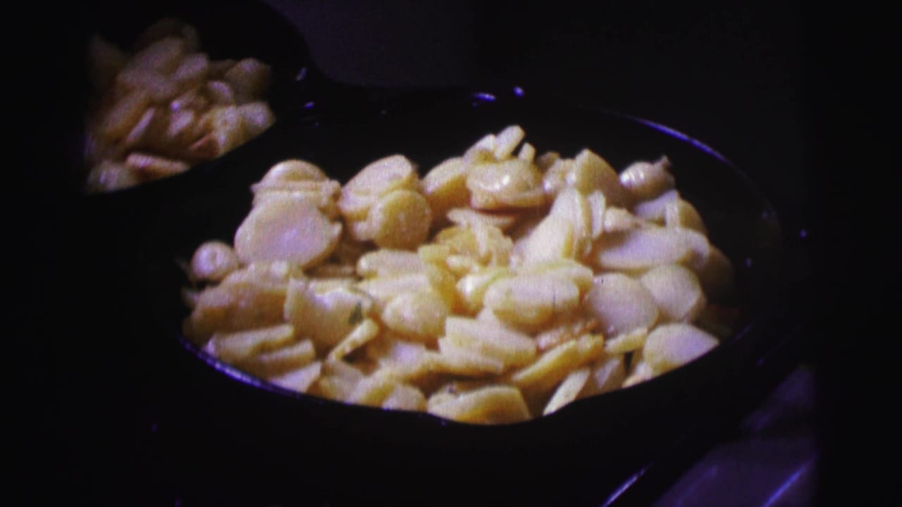 Brazil 1967 home-movie frame of sliced potatoes cooking in a black pan, with soft focus and dark surrounding shadows.