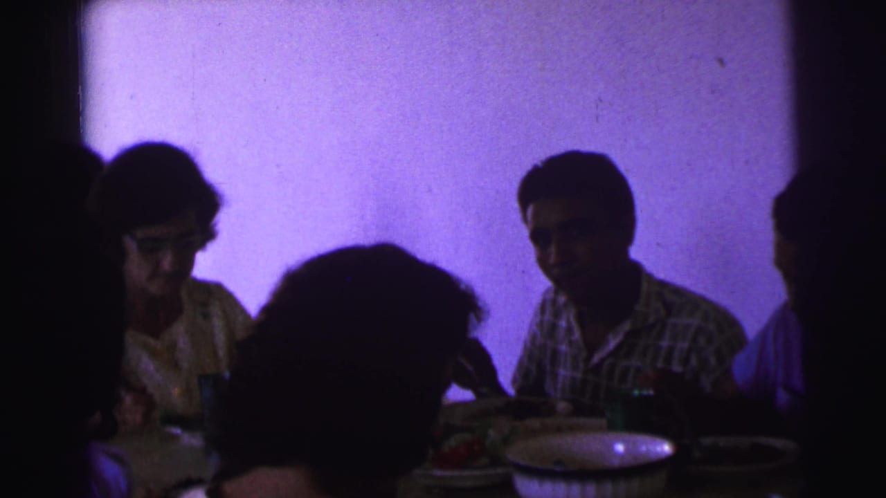 Brazil 1967 dinner scene with seated adults, tableware, food, and a strong purple cast from the film or lighting.