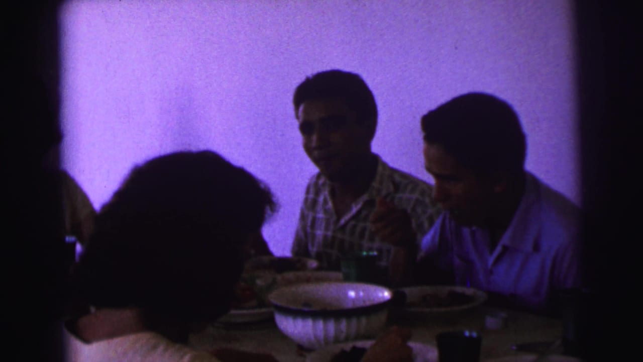 1967 Brazil home-movie frame showing men at a family meal, partially obscured by foreground silhouettes.