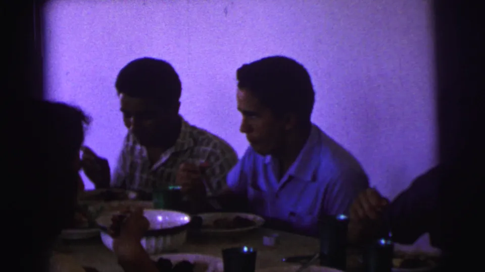 1967 Brazil dining-room frame with two men at the table, food dishes, cups, and low purple 8mm color.