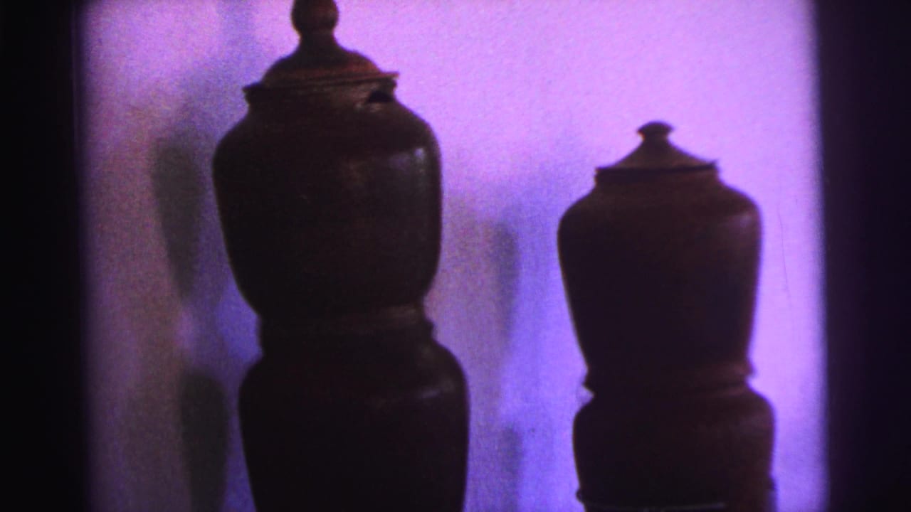 Two lidded brown pots remain centered against a purple-toned wall with heavy shadow.