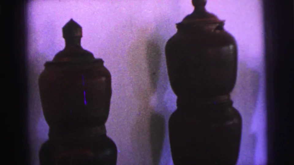 1967 Brazil 8mm frame showing two dark, bulbous lidded vessels on display against purple interior lighting.