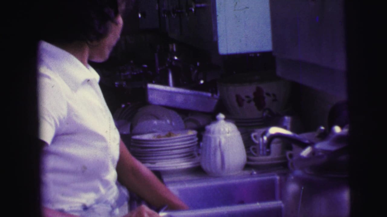 Woman at a sink beside plates, a teapot, and kitchen fixtures.