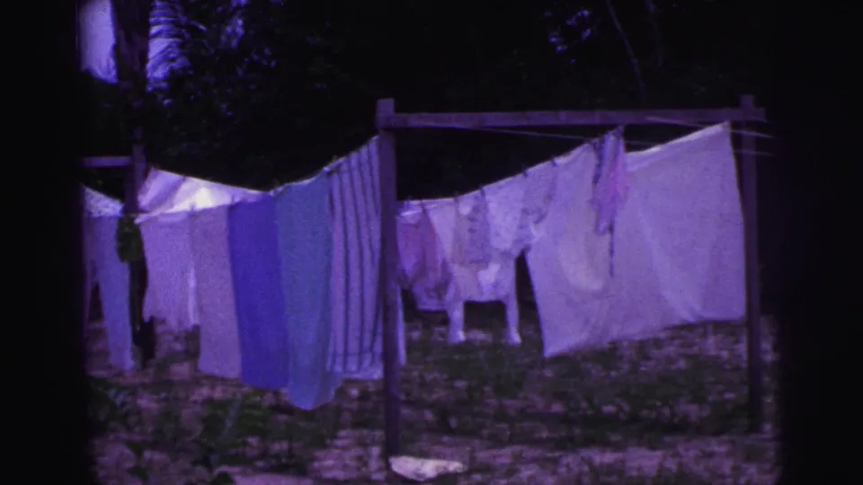 1967 Brazil home-movie frame showing sheets and garments drying on a clothesline in an outdoor yard.
