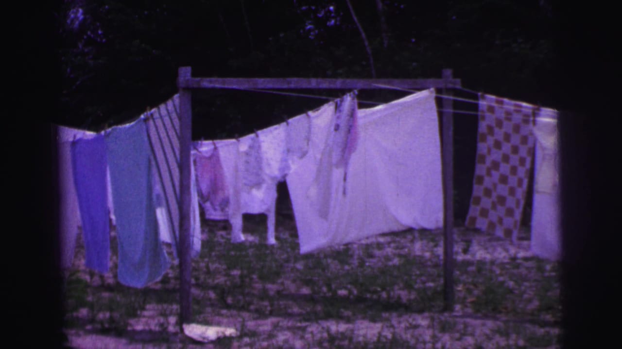 Laundry hangs from a clothesline between wooden posts in an outdoor yard.