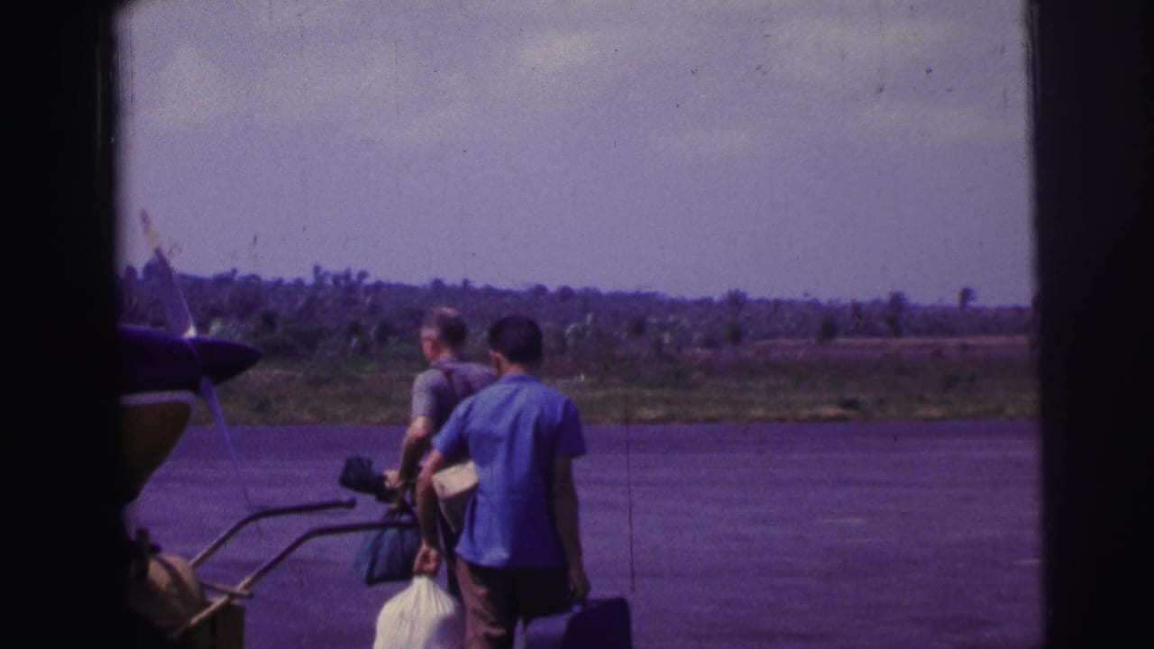 In 1967 Brazil, two men walk across a tarmac with luggage beside a parked small propeller plane.