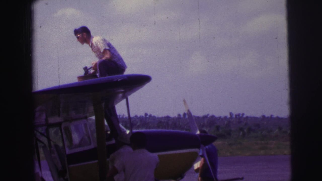 Man crouches on top of a small aircraft while another person works below near the nose.