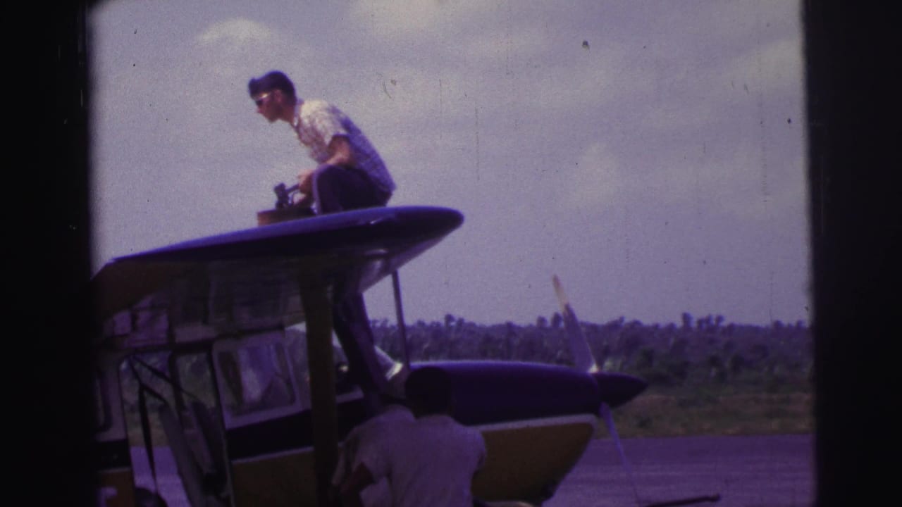 Man sits or crouches on the aircraft roof area with the nose and propeller visible below.