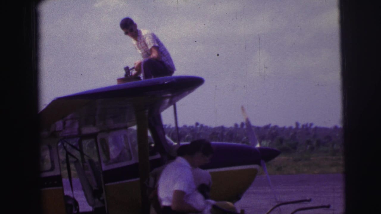 1967 Brazil 8mm frame showing two men around a small aircraft, one above the cabin and one below near the fuselage.