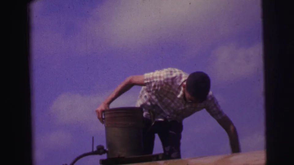 1967 Brazil frame showing the man bending beside a metal can as he reaches toward the fuel hose outdoors.
