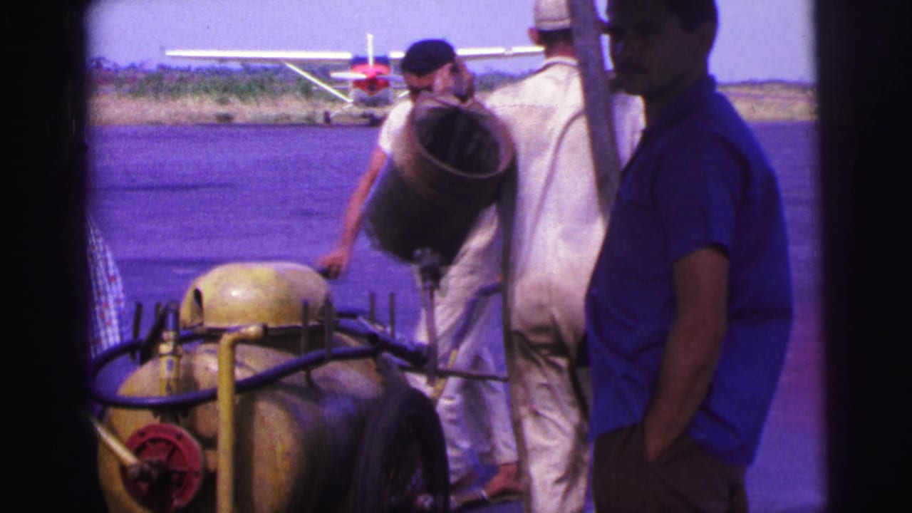 1967 Brazil airfield frame with workers moving ladder and fuel equipment in front of a red-and-white small plane.