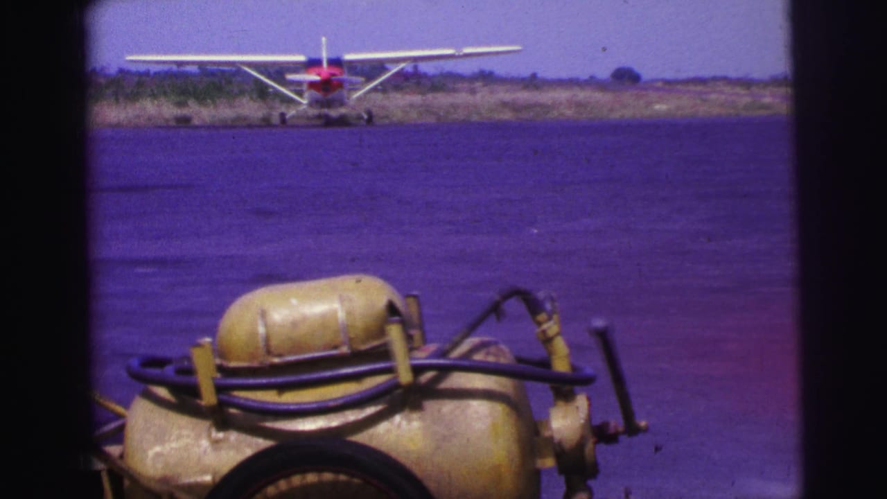 Yellow fuel cart in the foreground with a red and white seaplane beyond it on a tarmac.