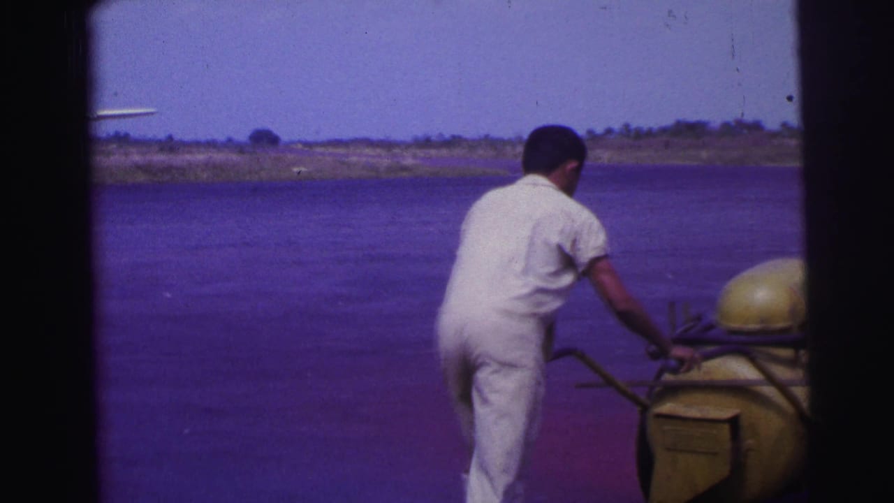 Man continues pushing the yellow fuel cart across the open airfield area.