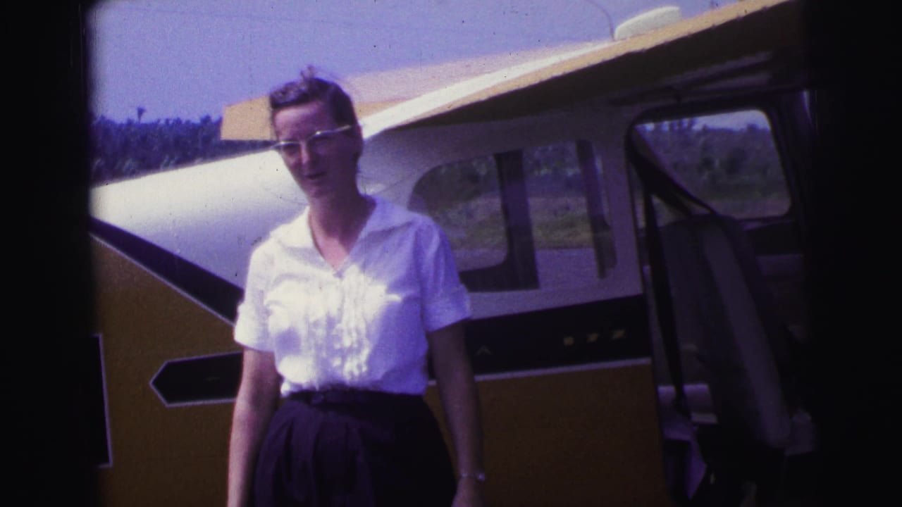 Woman in glasses standing beside a yellow-and-white aircraft at an airfield.