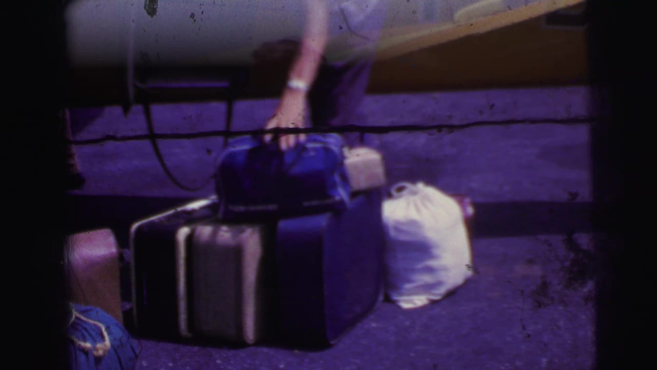 1967 Brazil home-movie frame showing luggage gathered beside a yellow aircraft as a person reaches down near the bags.