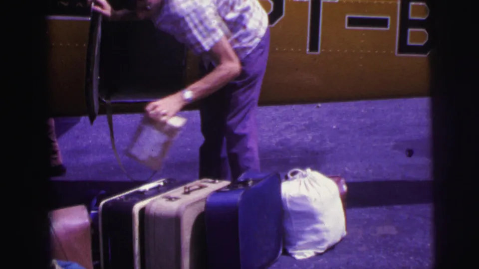 1967 Brazil frame showing a man handling a small box above vintage suitcases beside the open door of a yellow aircraft.