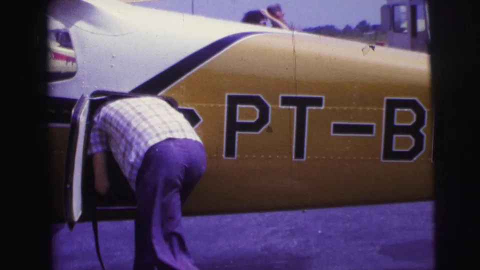 The man continues loading the small airplane, framed close to the yellow fuselage and large partial PT-B registration lettering.