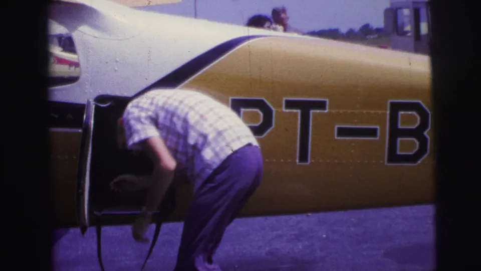 A man in period casual clothing reaches near the open compartment of a yellow-and-white airplane in 1967 Brazil footage.