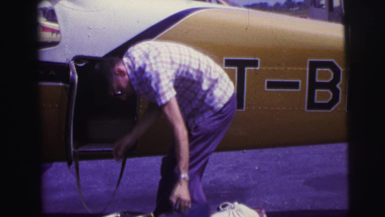 Man bends beside an open yellow and white small plane with a bag on the tarmac.