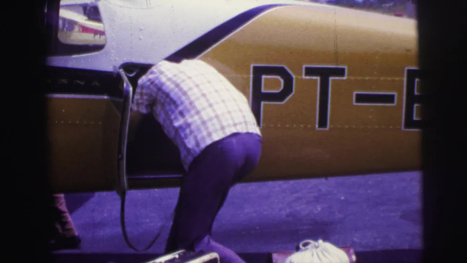 The man leans into the open aircraft compartment while large partial registration letters are visible on the yellow fuselage in the close 8mm frame.
