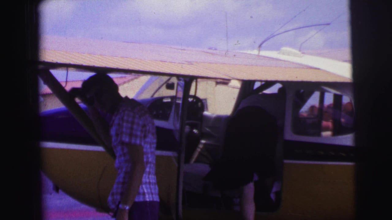 Man in a checkered shirt beside an open small propeller plane door.