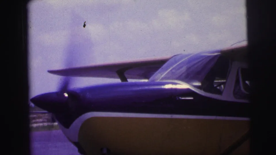 Small fixed-wing aircraft in blue and yellow livery appears beside runway pavement in 1967 Brazil home-movie footage.