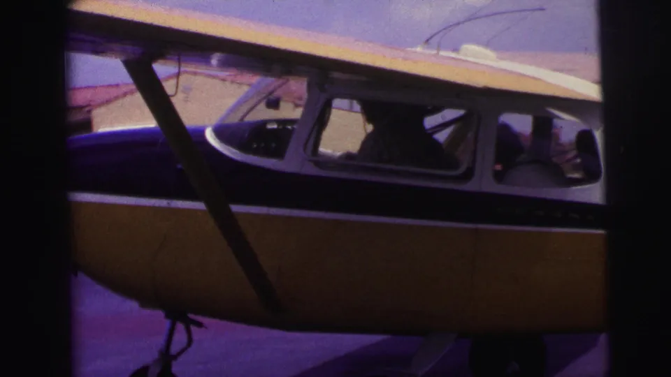 1967 Brazil 8mm frame with a side view of a small high-wing propeller airplane, cockpit windows, strut, and landing gear.
