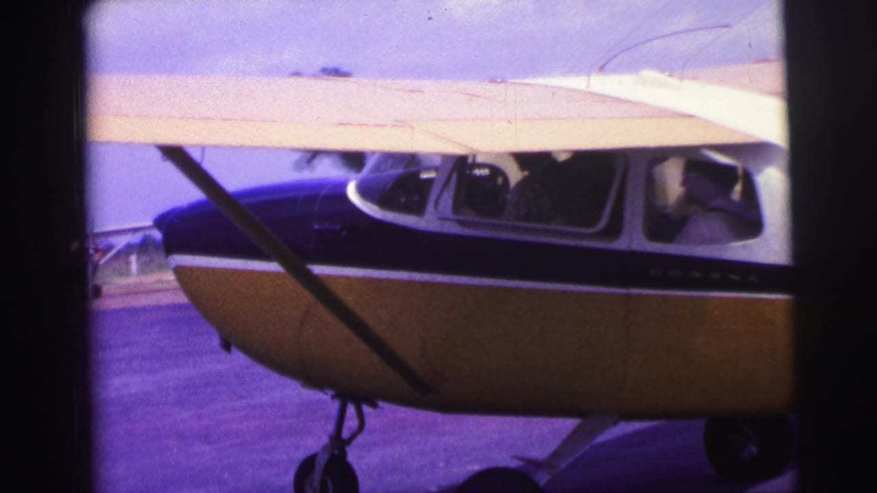 Yellow and blue high-wing airplane seen from the side on a runway.